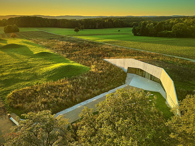 Das Gebäude des Heidengrabenzentrums auf einer Wiese, neben dem Grabhügelfeld bei Sonnenaufgang im Sommer.