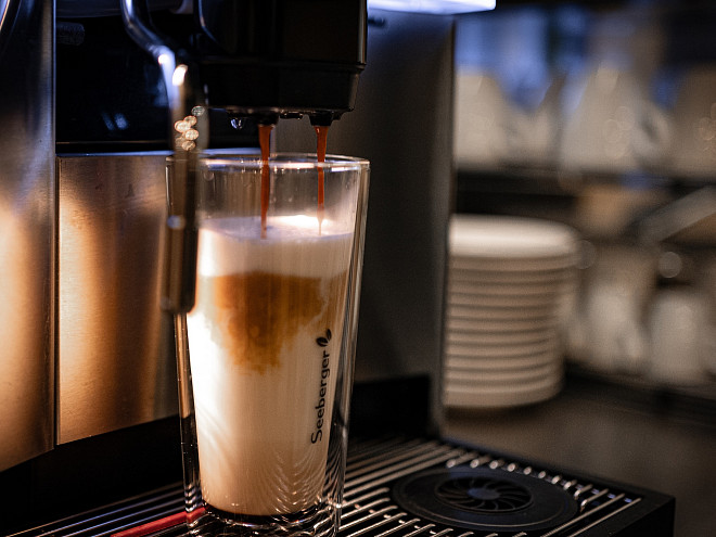 Ein Thermoglas mit Kaffee und Milch, das unter einer Kaffeemaschine gerade befüllt wird.