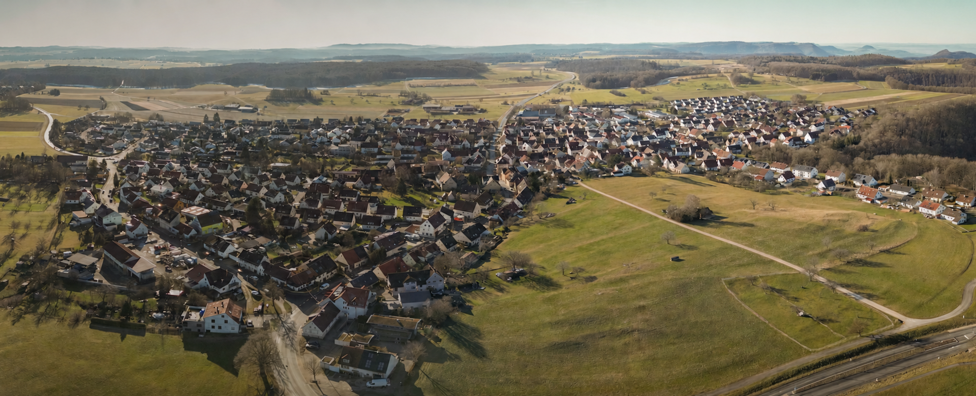 Eine Luftaufnahme einer kleineren Ortschaft, umgeben von Wald und Wiese.