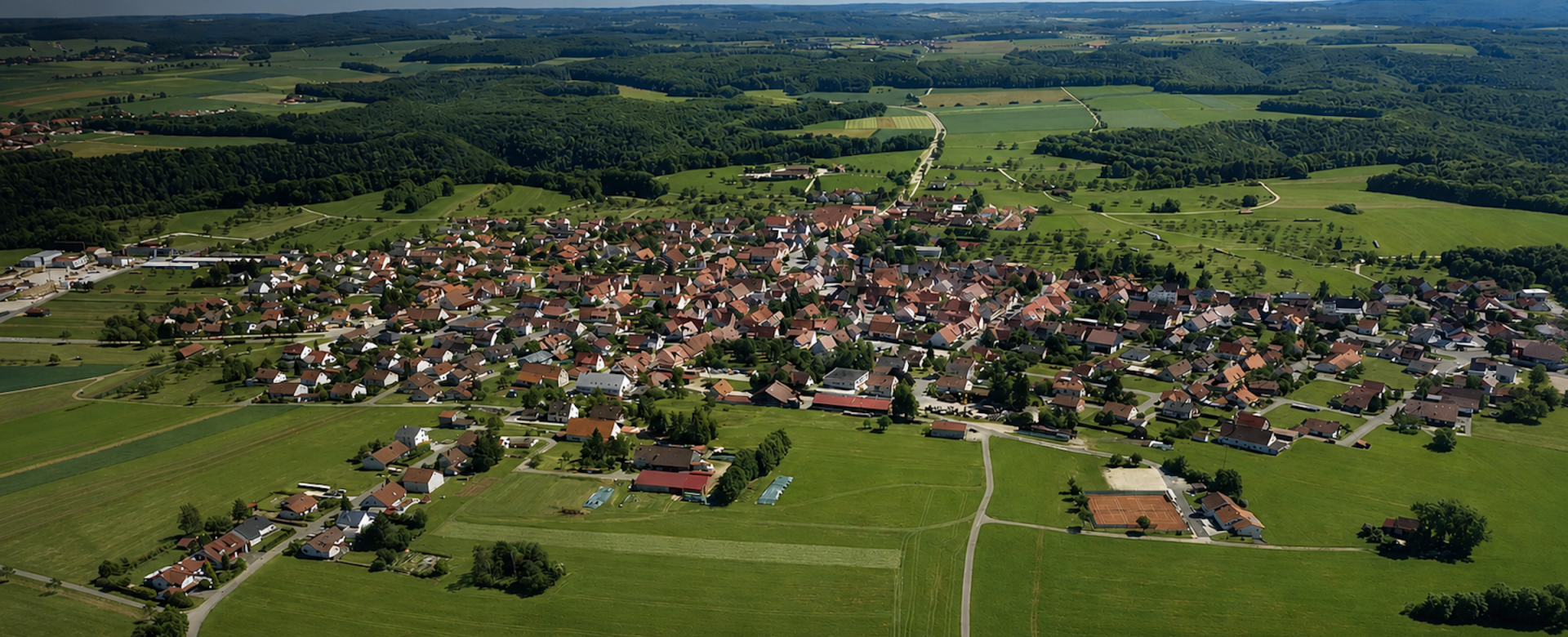 Eine kleine Gemeinde aus der Luft, umringt von Wald und Wiese.