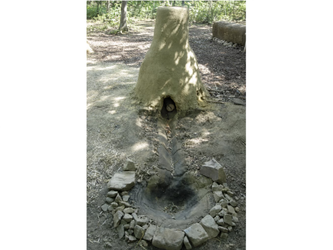 Ein Nachbau eines keltischen Rennens aus Lehm auf dem Boden im Hintergrund Wald der Boden ist sandig, erdig.