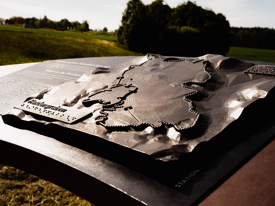 Eine Bronzeskulptur im Außenbreich, die eine schematische Siedlungsstruktur zeigt.