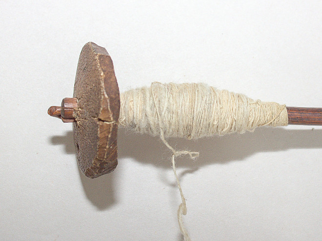Spinnwirtel aus Knochen mit zentraler Bohrung, als einzelnes Objekt fotografiert.