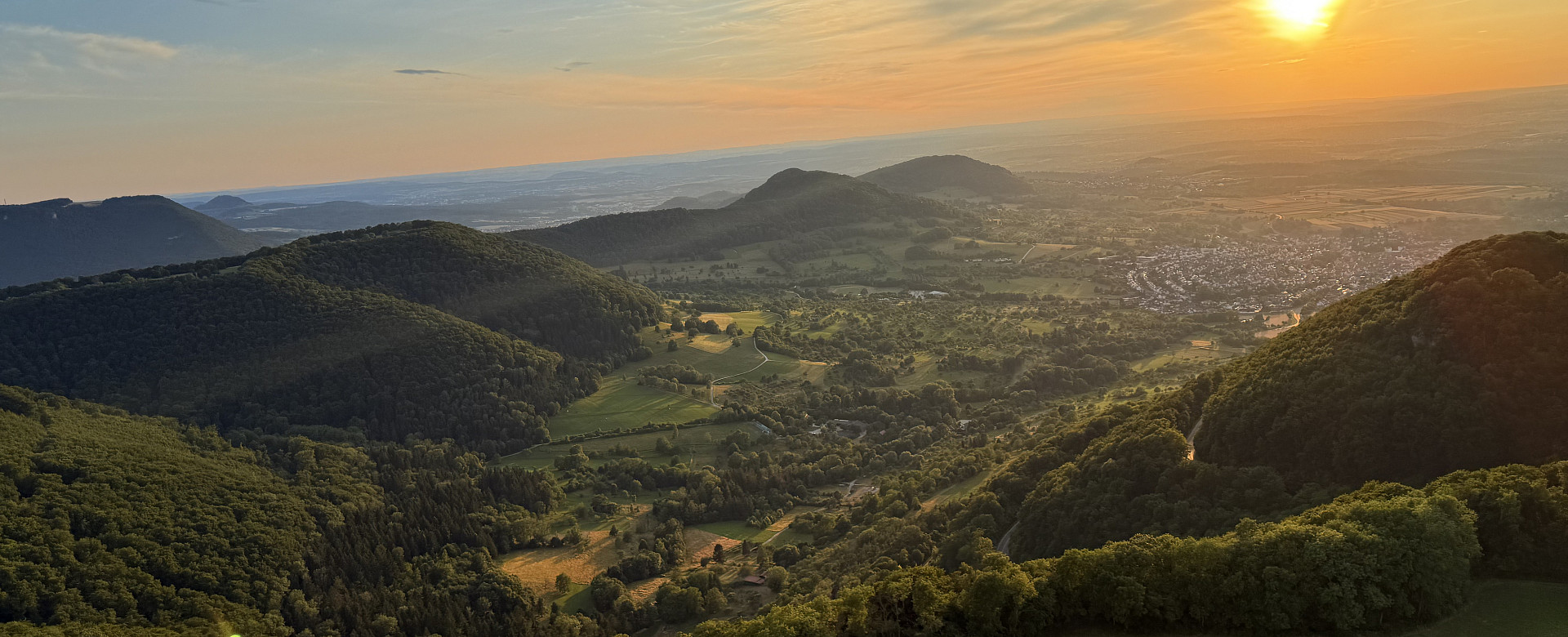 Weitläufiger Blick über die bewaldeten Hügel und Täler des Albtraufs. Die tief stehende Sonne taucht die Landschaft der Schwäbischen Alb in warmes Abendlicht.
