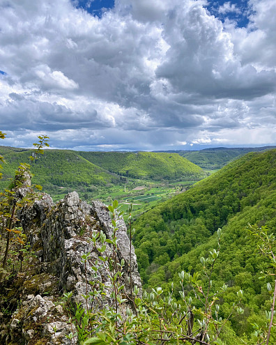 Von einem felsigen Aussichtspunkt fällt der Blick über das grüne Lenninger Tal. Bewaldete Hänge und beeindruckende Wolken prägen die Landschaft der Schwäbischen Alb.