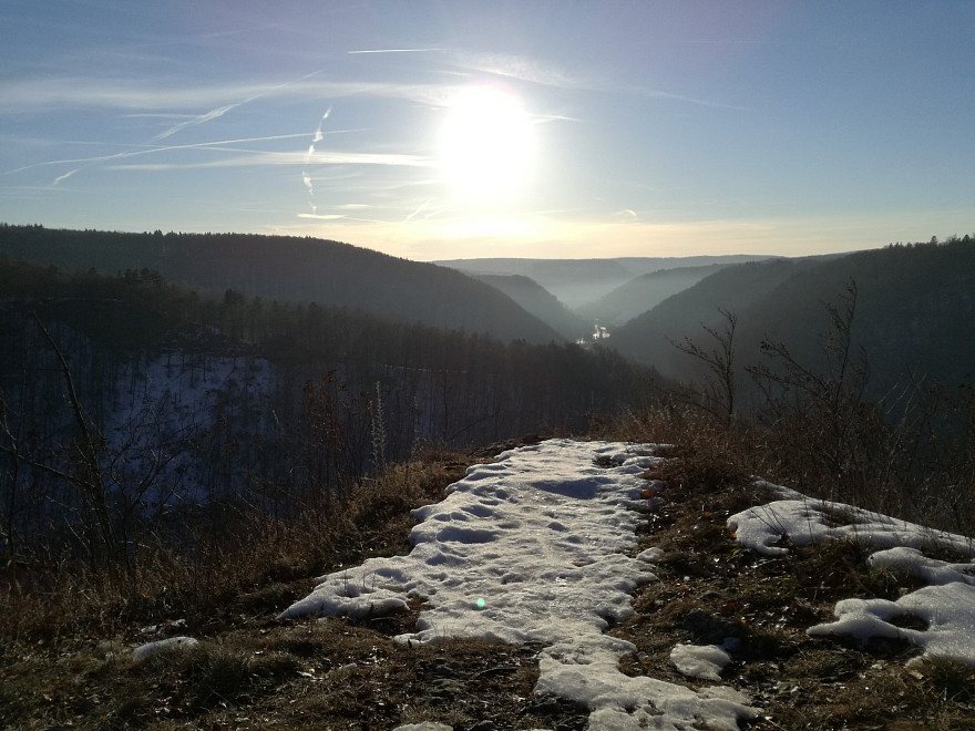 Ein verschneiter Aussichtspunkt eröffnet den Blick über bewaldete Täler des Albtraufs. Die tief stehende Wintersonne beleuchtet die Landschaft.